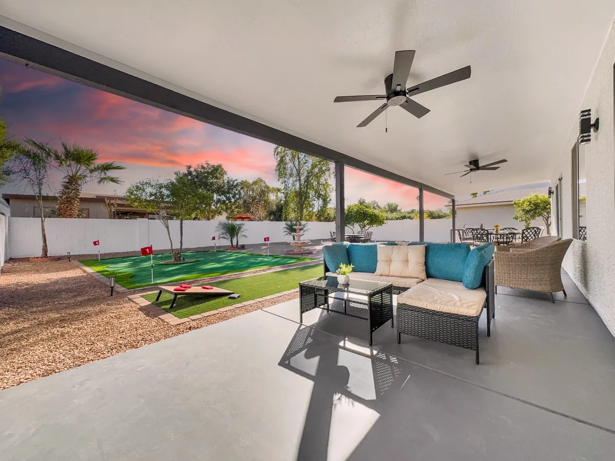 This image captures an inviting outdoor seating area set on a lush green lawn, with flags visible for backyard games, palm trees providing a resort-like atmosphere, and a glowing sunset sky in the background. The setting is ideal for both relaxation and entertainment, blending comfort with the natural beauty of the yard.