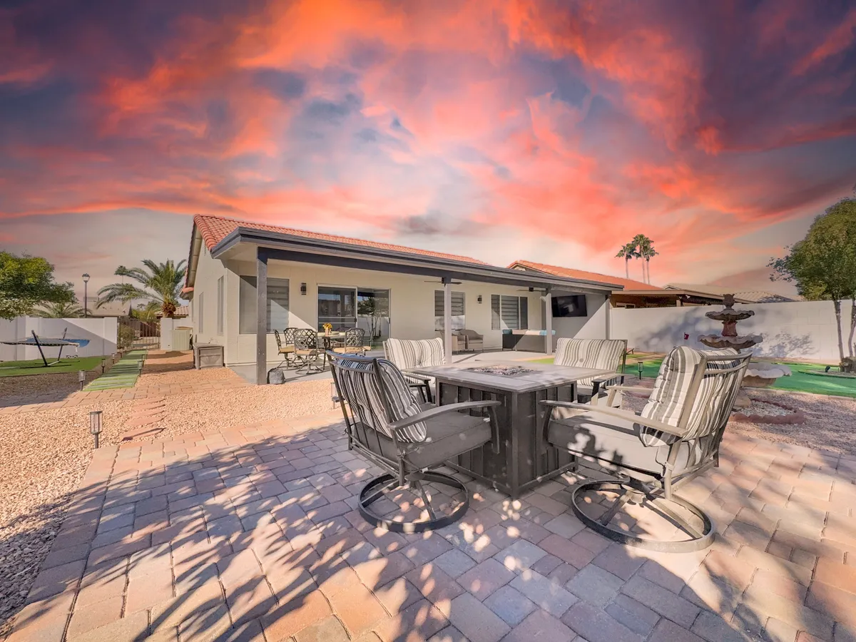 An elegant outdoor dining area with a stylish table and comfortable seating, adjacent to a soothing fountain and beautifully manicured landscaping. The sky is painted with sunset colors, enhancing the serene, resort-like ambiance.