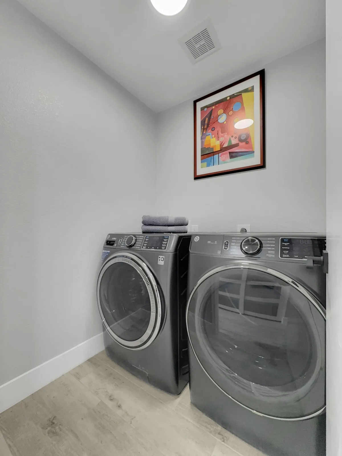 This interior image captures a modern laundry room with a washer and dryer, colorful artwork, and a neatly stacked towel, creating a functional yet inviting atmosphere.