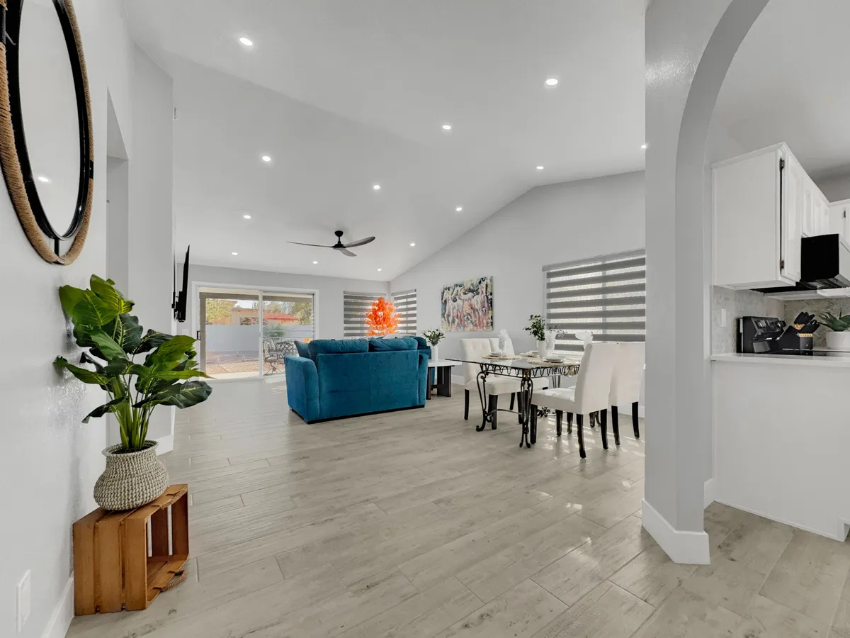 An open living and dining space with a blue sofa, a wooden dining table, a lush green plant, and vibrant artwork adding cheerful energy. The setup encourages casual gatherings and shared meals, seamlessly linking the lounge and dining areas.