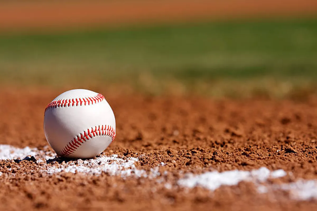 A well-maintained baseball field with a dirt infield and crisp white chalk lines, bathed in warm sunlight. The scene captures the anticipation of a game, evoking a sense of community gathering and outdoor activity.