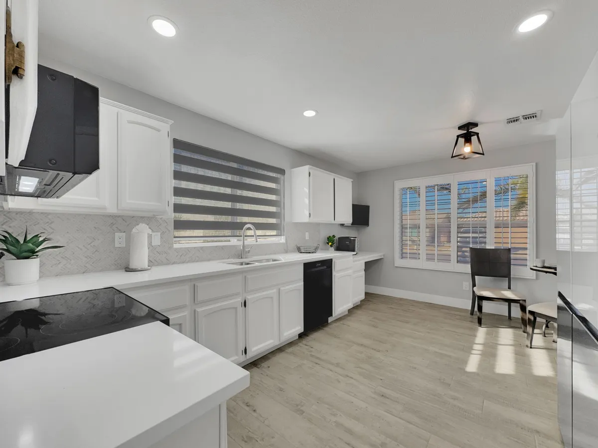 A bright, inviting kitchen featuring clean white cabinetry, modern appliances, a spacious kitchen island, and a dining area bathed in natural light. The space is clearly designed for both cooking and gathering, with plenty of room for guests to mingle or enjoy a meal.