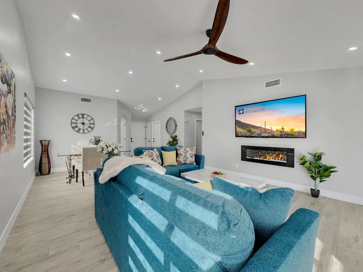 A spacious, modern living room featuring a large turquoise sofa, a sleek wall-mounted TV above a contemporary fireplace, and tasteful decorative wall art. The space radiates comfort and style, perfect for relaxing, socializing, or enjoying movie nights.