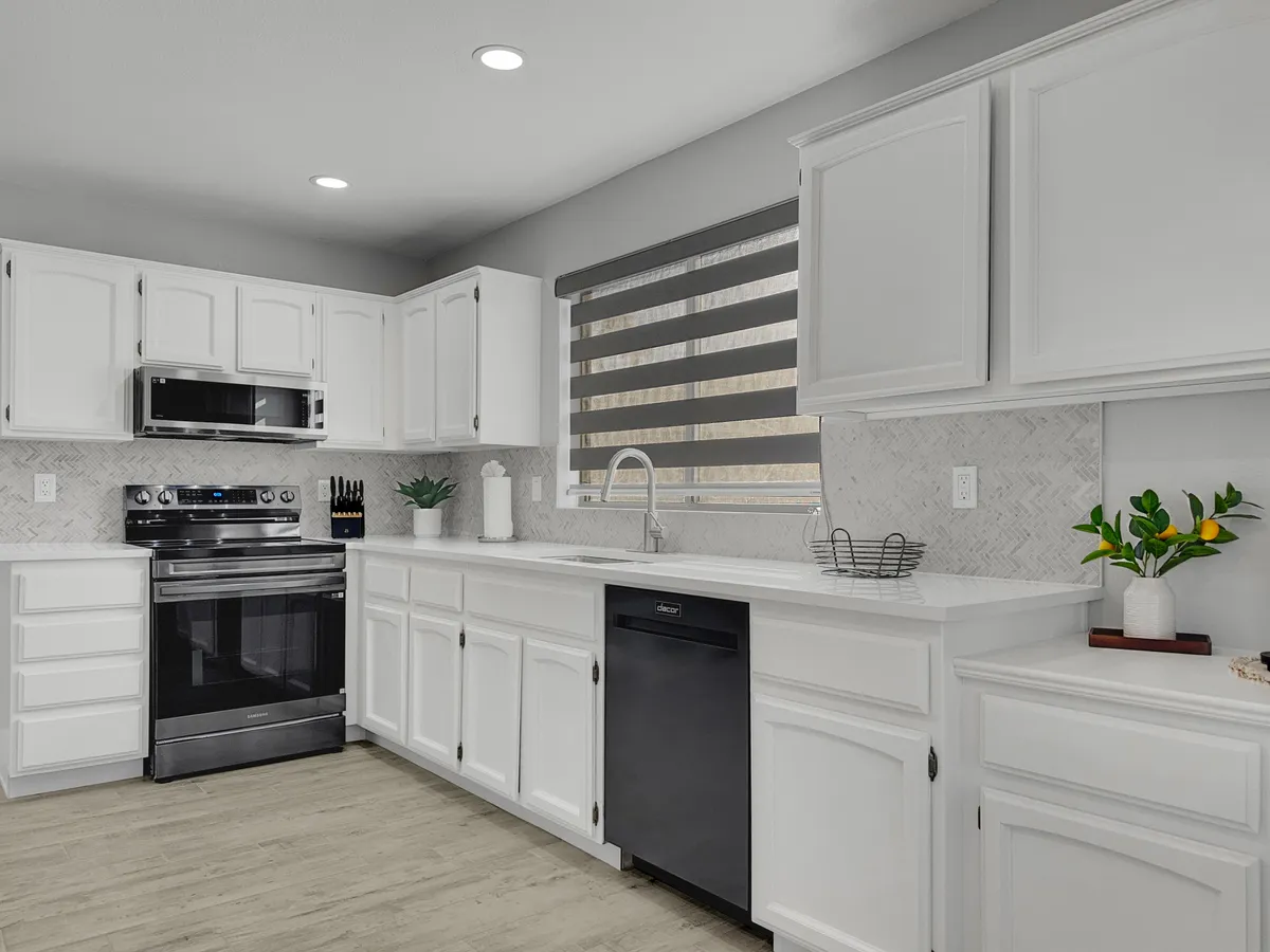 A bright, remodeled kitchen with white cabinetry, stainless steel appliances, a striking herringbone backsplash, a window with patterned shades, and touches of greenery. Ample counter space and storage options make the kitchen both functional and inviting.