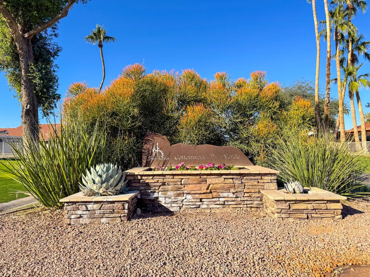 A beautifully landscaped entryway featuring prominent stone signage for the community, surrounded by a lush arrangement of succulent plants, colorful flowers, and vibrant greenery. The image captures an inviting and well-maintained neighborhood entrance, setting a welcoming tone.