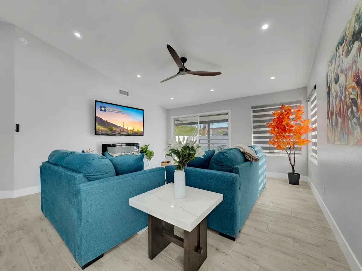 A cozy, contemporary living space with teal sofas, a white marble coffee table, a TV overlooking a mountain view, and vibrant artwork. The setting is perfect for relaxed socializing, movie nights, or casual conversations among friends.