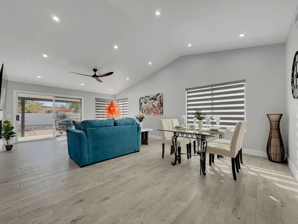 A spacious open-plan living and dining area anchored by a stylish blue couch, a family-sized dining table, contemporary wall art, and lush indoor plants. The area exudes warmth and hospitality, visually supporting activities like relaxing, entertaining guests, and family meals.